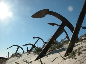 Six rusted anchors, standing in sand.